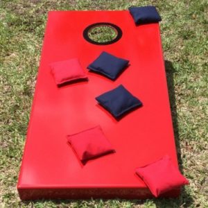 A red bean bag toss game on the grass.